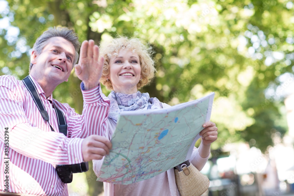 Naklejka premium Happy middle-aged couple holding map in city