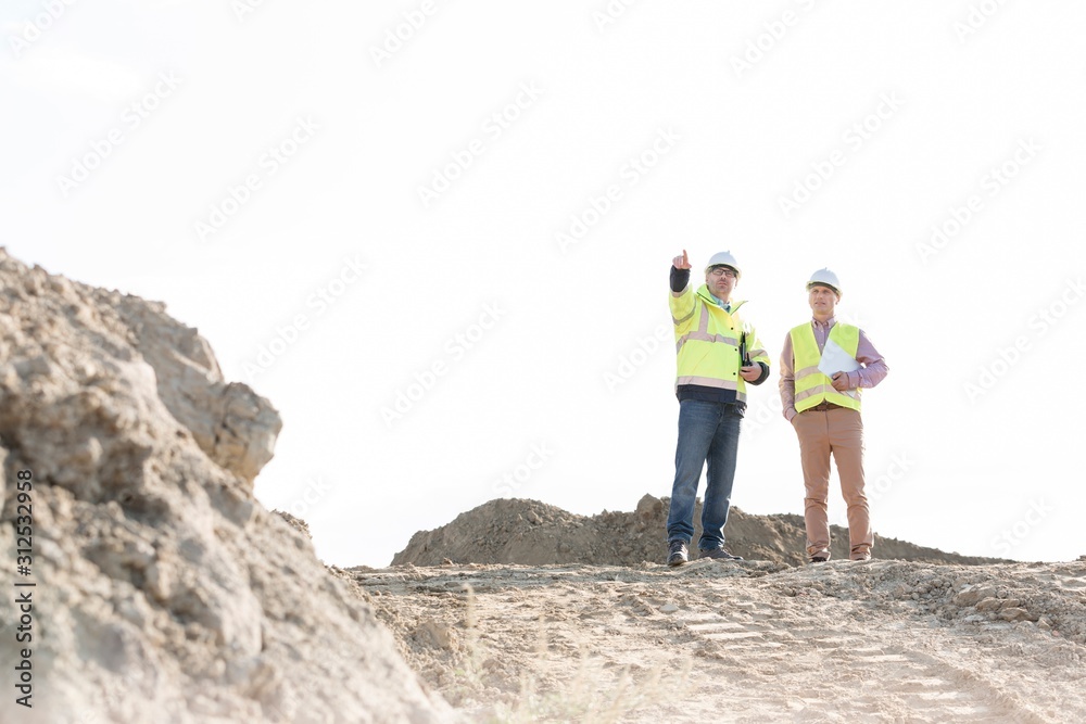 Supervisor discussing with colleague at construction site against clear sky Supervisor discussing with colleague at construction site against clear sky