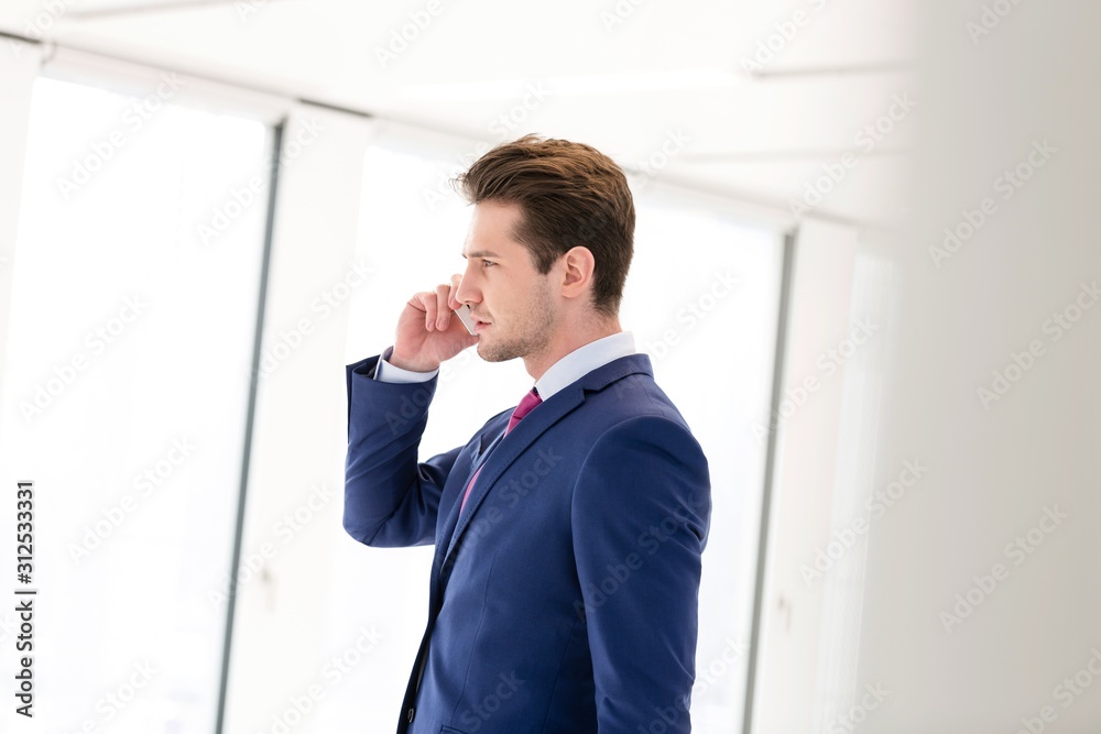 Side view of young businessman using mobile phone in new office Side view of young businessman using mobile phone in new office