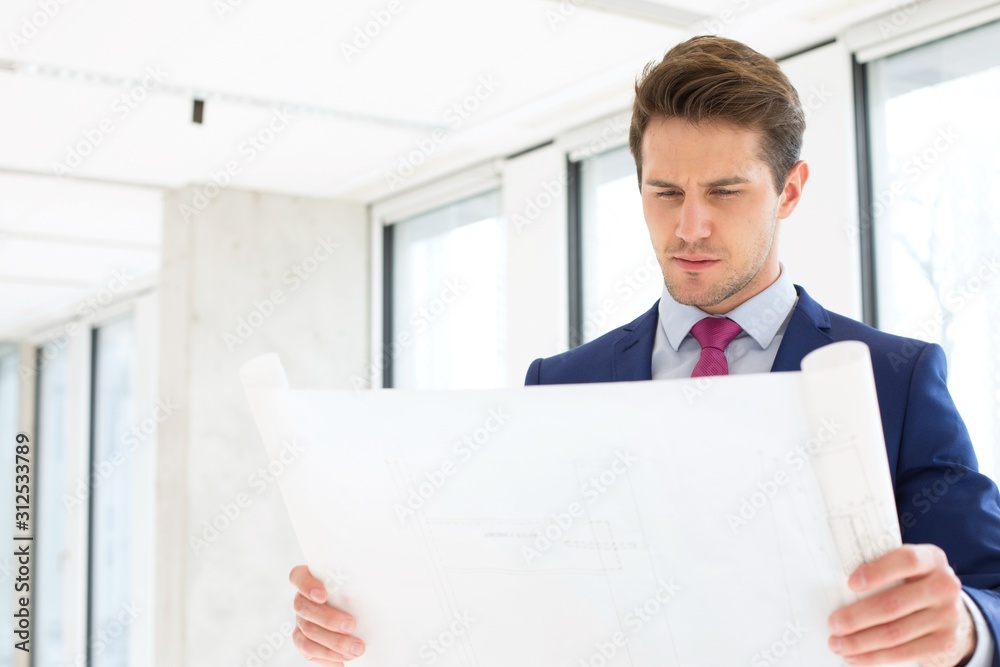 Confident young businessman reading blueprint in new office Confident young businessman reading blueprint in new office