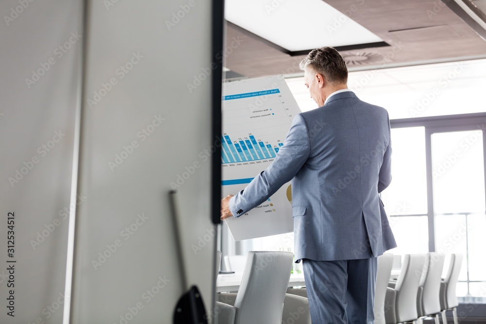 Rear view of businessman analyzing graph on chart in board room Rear view of businessman analyzing graph on chart in board room
