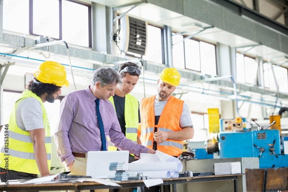 Supervisor with workers examining blueprints at table in industry Supervisor with workers examining blueprints at table in industry