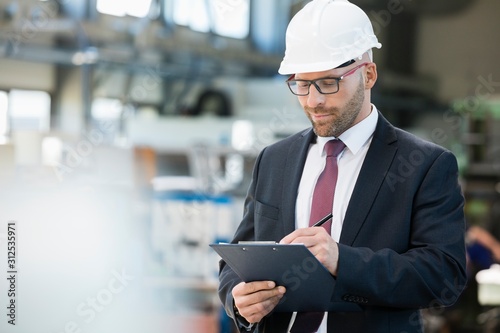 Mid adult businessman writing on clipboard in metal industry