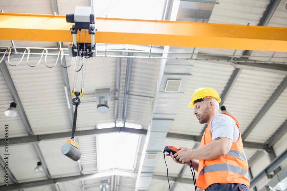 Low angle view of manual worker operating crane lifting steel in industry