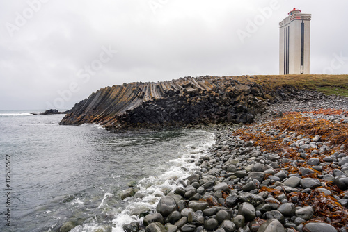 Kalfshamarsvik lighthouse in the western part of Iceland during rainy weather. Ocean view from the beach towards basalt colums and lighthouse. Architecture, icelandic and traveling concept. photo