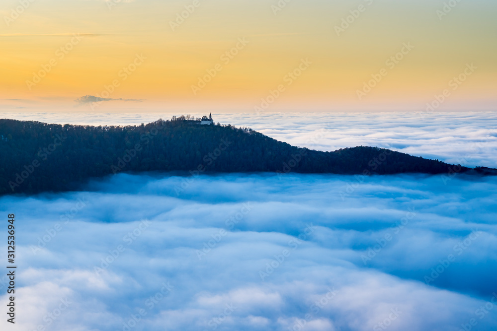 Germany, Magical aerial view above foggy cloudscape in valley of swabian jura nature landscape at sunset with orange sky near stuttgart with view to castle teck