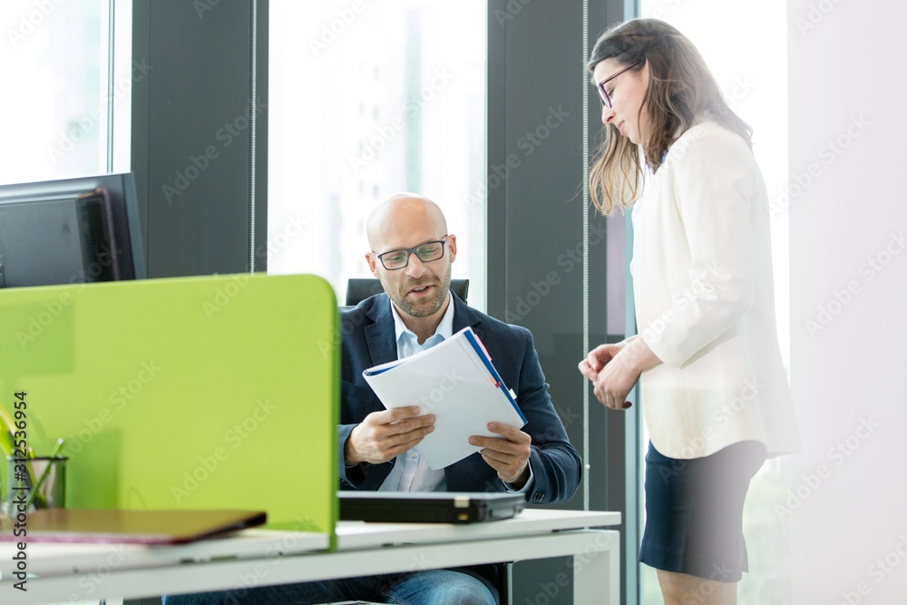 Young businesswoman standing by businessman reading book at office Young businesswoman standing by businessman reading book at office