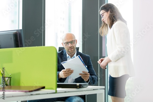 Young businesswoman standing by businessman reading book at office © moodboard