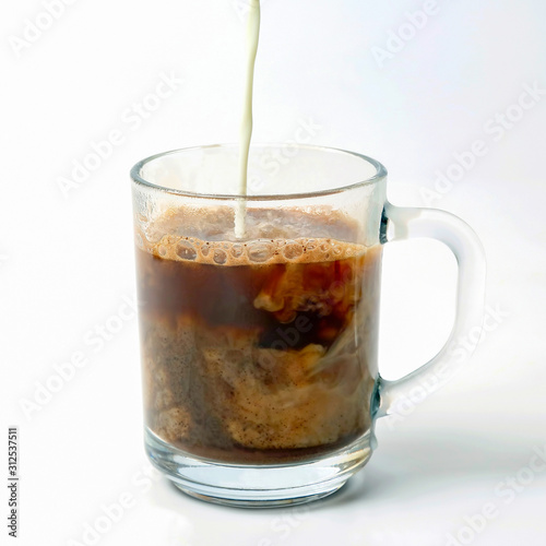 milk poured into a transparent cup of black coffee