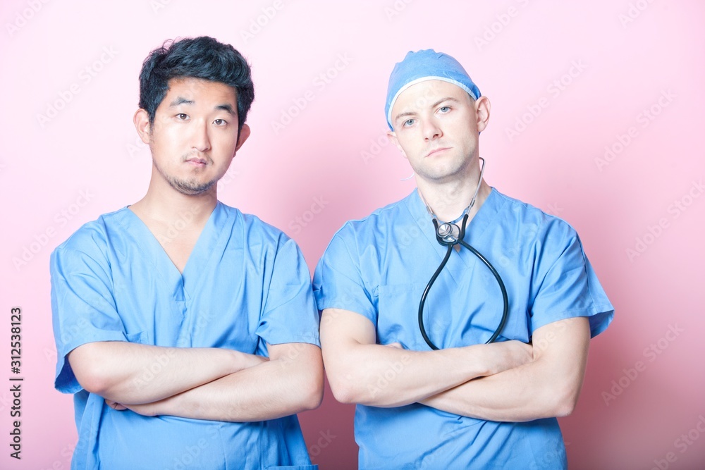 Portrait of two male surgeons standing with arms crossed over pink background Portrait of two male surgeons standing with arms crossed over pink background