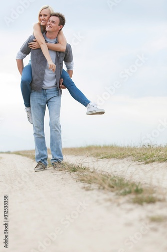 Young man piggybacking woman on trail at field