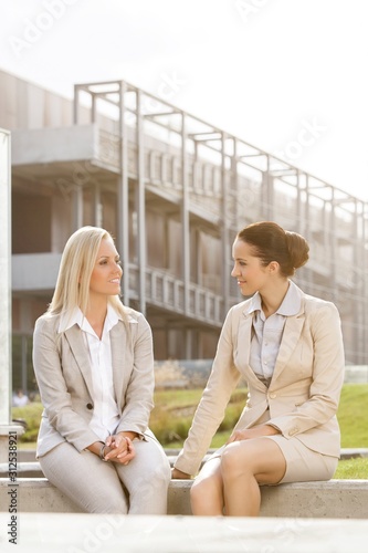 Young businesswomen looking at each other while sitting against office building