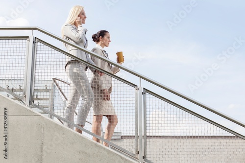 Profile shot of businesswomen moving down stairs against sky © moodboard