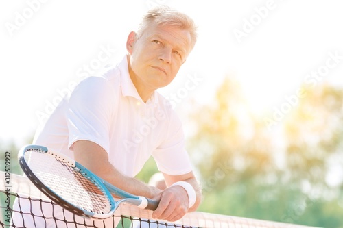 Tennis player holding racket while leaning on the net with yelow lens flare 