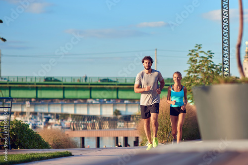 Modern woman and man jogging / exercising in urban surroundings near the river. © astrosystem