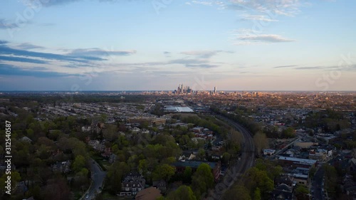 Aerial drone timelapse of the Philadelphia skyline with blue skies from the suburbs over green summer trees and Septa train tracks