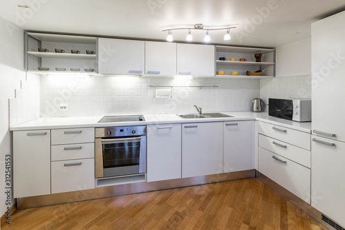 Kitchen in studio apartment. White interior. Wooden floor. White kitchen set.