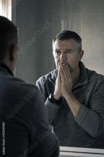 Man in grey polar fleece staring at himself in bathroom mirror