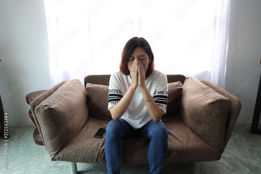 Asian woman stressful face with her hands cover of face. Short hair asian Woman feel lonely and sad sit alone on sofa bed in the living room Asian woman stressful face with her hands cover of face. Short hair asian Woman feel lonely and sad sit alone on sofa bed in the living room