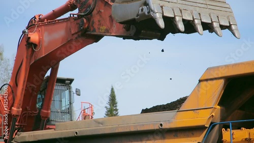 Close-up Red excavator digs an earth and loads into a yellow dump truck