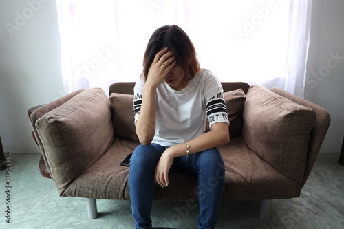 Asian woman stressful face with her hands cover of face. Short hair asian Woman feel lonely and sad sit alone on sofa bed in the living room © Snowhite