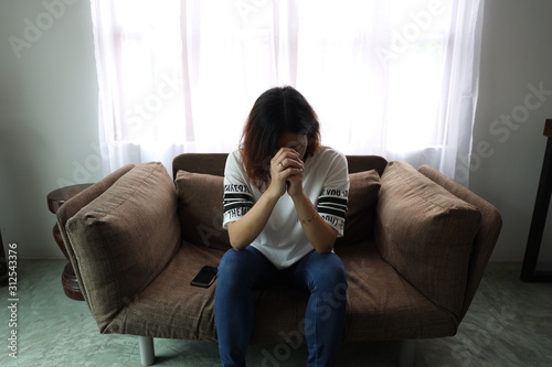 Asian woman stressful face with her hands cover of face. Short hair asian Woman feel lonely and sad sit alone on sofa bed in the living room