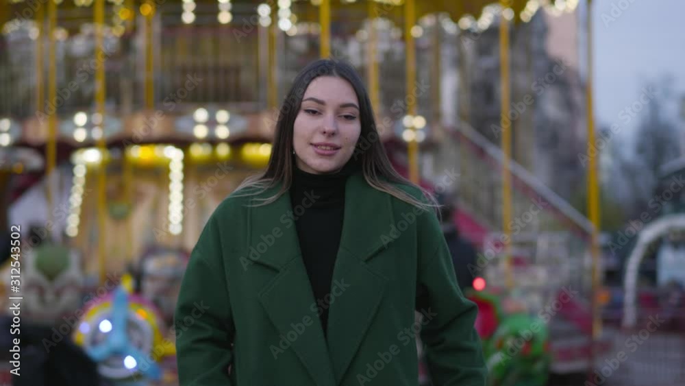 Portrait of beautiful Caucasian girl standing in front of colorful carousels and smiling. Young beautiful woman spending weekends on city market. Lifestyle, happiness, leisure. Portrait of beautiful Caucasian girl standing in front of colorful carousels and smiling. Young beautiful woman spending weekends on city market. Lifestyle, happiness, leisure.