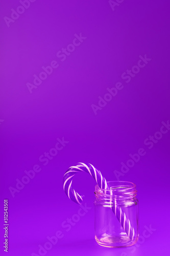 One Lollipop Candy cane in a glass jar on a purple background.