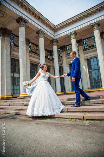 newlyweds stand near an old building with white columns. veil in the wind