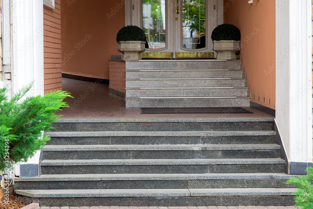 marble steps rise to the threshold of the hotel entrance with stone flowerpots with green bushes, close up. marble steps rise to the threshold of the hotel entrance with stone flowerpots with green bushes, close up.