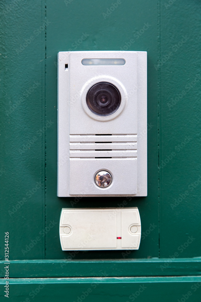 an intercom with a video camera and a microphone for voice communication with a card reader for access by a key card is installed on a green iron wall front view. an intercom with a video camera and a microphone for voice communication with a card reader for access by a key card is installed on a green iron wall front view.