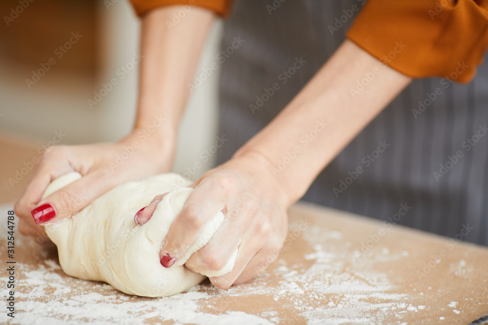 Close up of unrecognizable woman kneading batter while baking homemade pastry on kitchen table, copy space