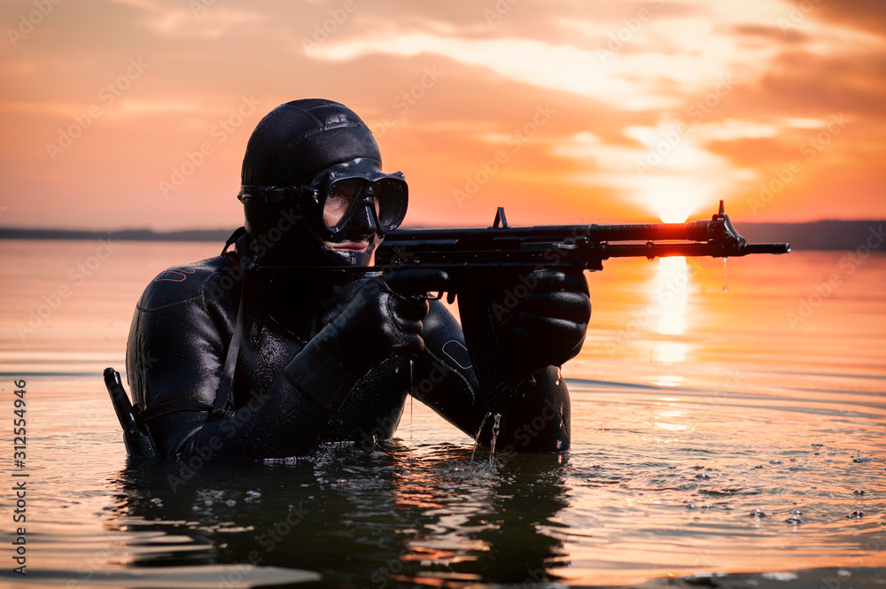 The marine comes out of the water and moves toward the target with weapons in hand. The concept of video games, advertising, instability in the world, country conflicts. - obrazy, fototapety, plakaty 