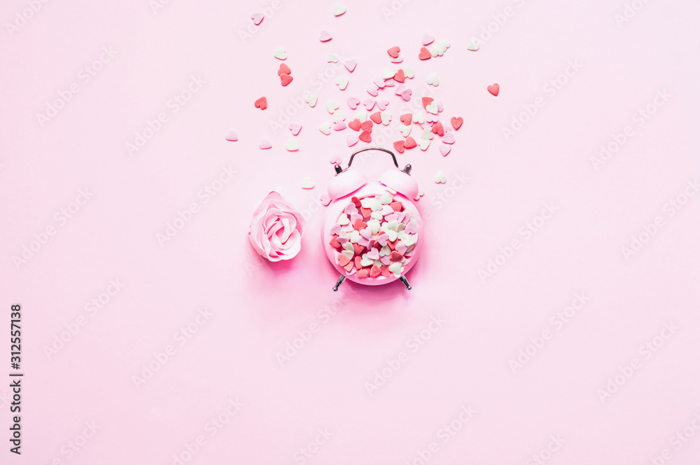 Valentines Day. Festive concept on pink background with heart shaped sweet confetti with alarm clock Valentines Day. Festive concept on pink background with heart shaped sweet confetti with alarm clock