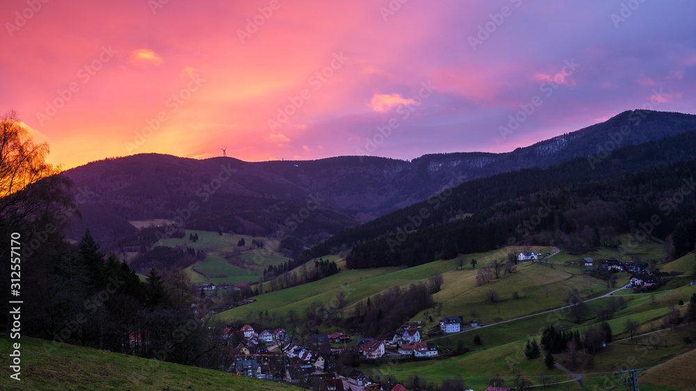 Germany, Magical red sky over mountains and valley surrounding black forest village early in the morning in winter