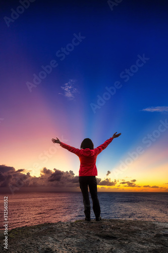 Adventurous Girl with open hands on a Rocky Ocean Coast enjoying the beautiful view of the Colorful Sunset. Image Composit. Adventure, Travel, Explore, Freedom Concept.