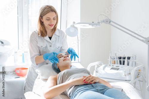 Woman professional doctor beautician applies a mask on a patient's face for skin care. Cosmetic procedures for skin rejuvenation and nutrition photo