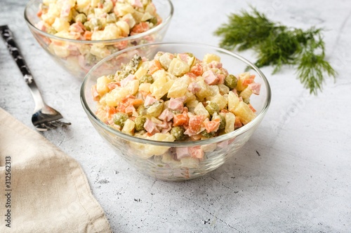 Russian traditional salad Olivier with boiled vegetables, in a glass salad bowl on the table. Gray background.
