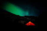 Burning red tent in night with polar lights