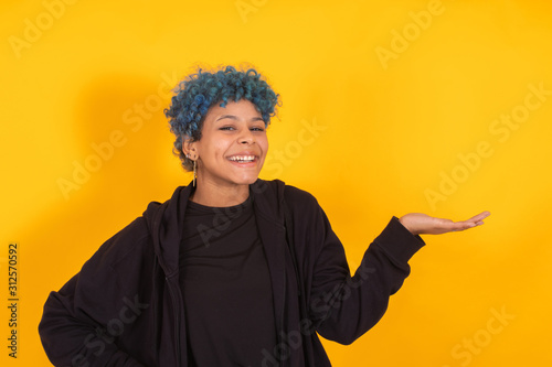 young african american girl or woman isolated on yellow background with expression and blue hair © carballo