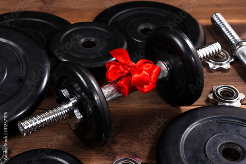 Fototapeta Naklejka Na Ścianę i Meble -  gift - dumbbells tied with a red ribbon on a dark wooden table along with sports equipment
