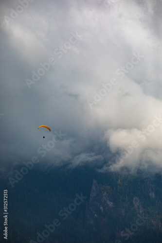 A paraglider flying over glacial water on a foggy day in the mountains