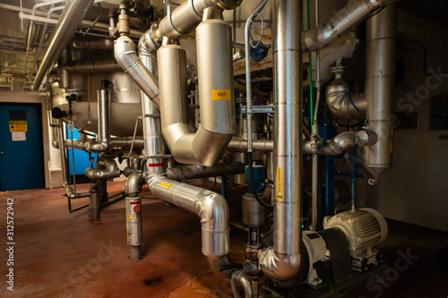 the piping system under tanks and vessels, metallic stainless steel pipes and pumps, with signs of hot caution, wort pre-syrup, syrup injection, steam