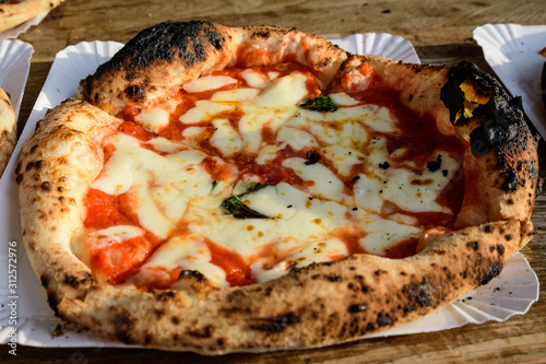 Tasty fresh home made margherita rustic pizza with tomatoes and mozzarella soft cheese, on a wooden table, displayed for sale at a street food market, in direct sun light, photographed with soft focus