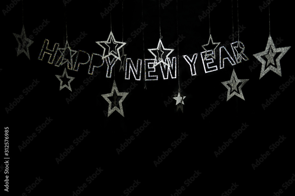 Fototapeta premium Happy New Year message in glittery bokeh silver rainbow letters strung from a banner hanging across black night sky with stars