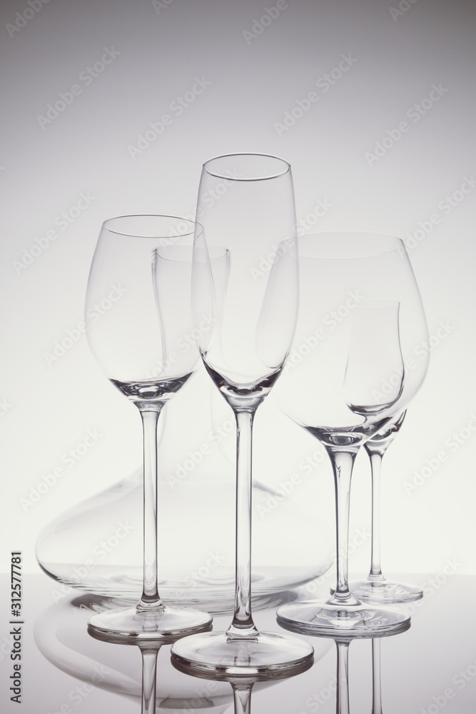 Glassware selection with wine, champagne, liquour glasses and decanter on the light background.. Fine cristal glassware concept. Vertical in light cold toning