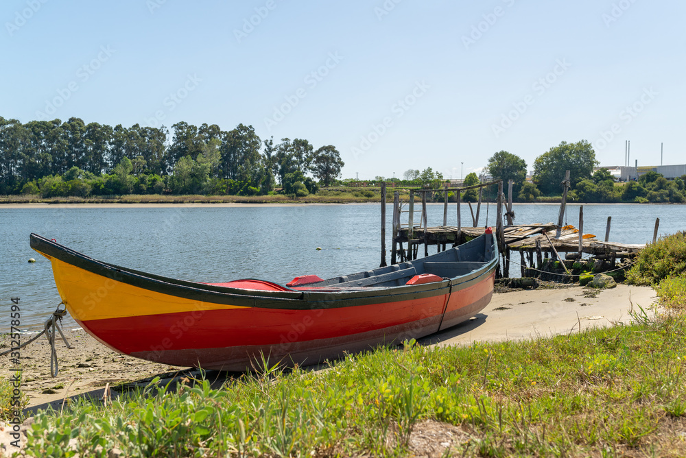 Traditional fishing boat on the shore of Ria de Aveiro near a small wooden jetty. Portuguese landscape.