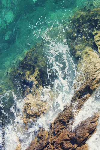 Green and blue sea water with white foam from the waves crashing on the rocks