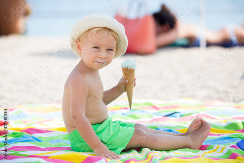 Sweet blonde toddler boy, eaiting ice cream on the beach