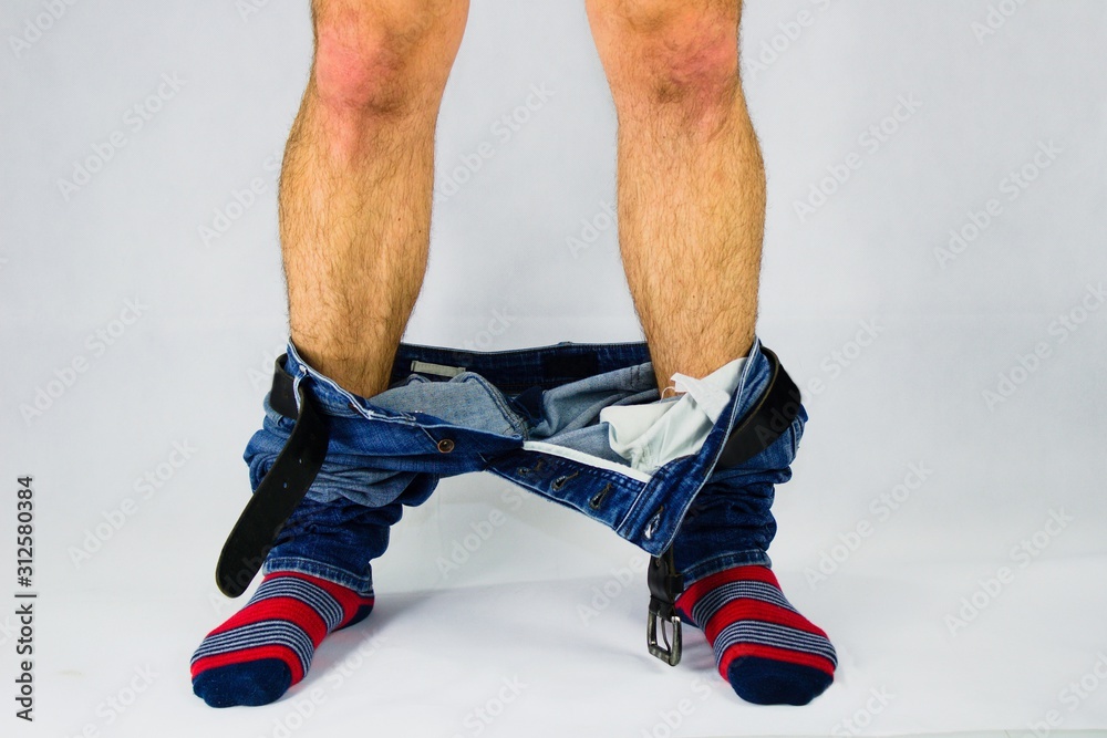 Man has his pants and underwear down at the ankles.Man in front of white  background has pants pulled down. Stock Photo | Adobe Stock